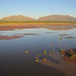 Water in desert with mountains in background.