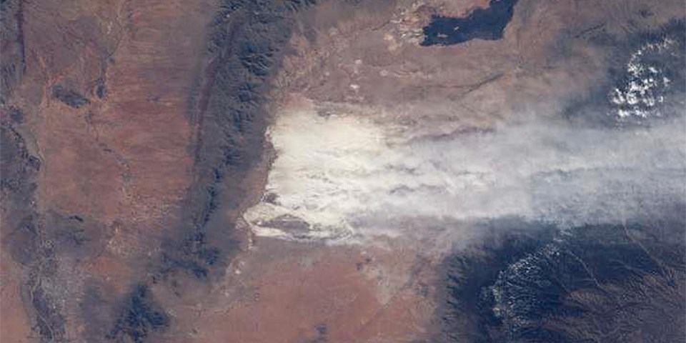 An image from space of white sand and dust being blown over a mountain range