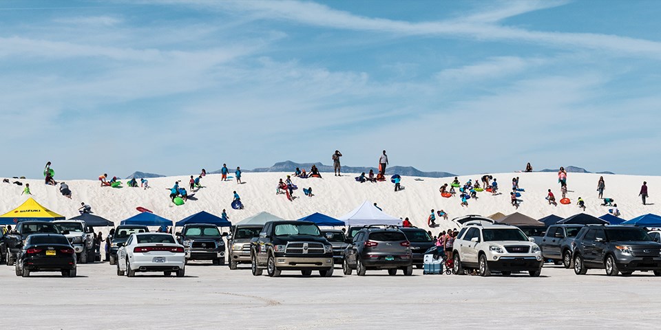 Vehicles parked in front of dunes covered with people