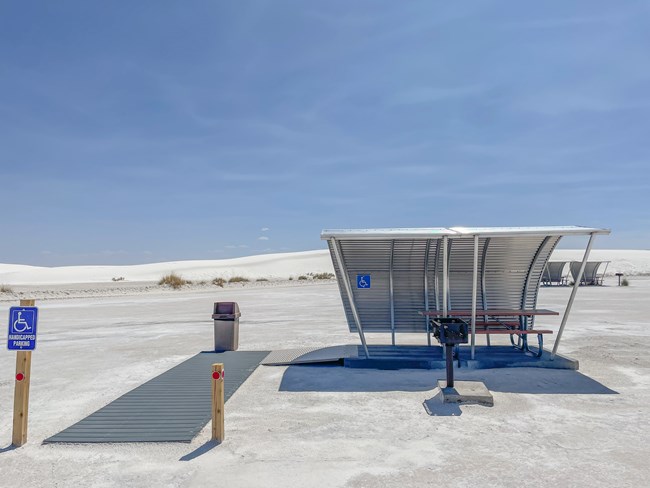 a picnic table under metal shade structure sits upon pedestal with ramps leading to it.