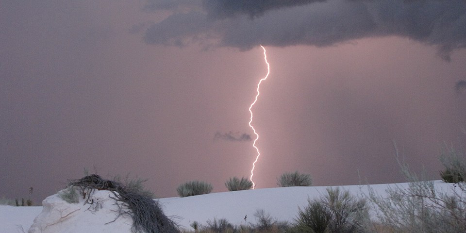 Pink sky with a bright lightning bolt hitting the white sand