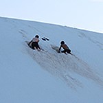 Two boys on a steep slope digging holes in the sand.
