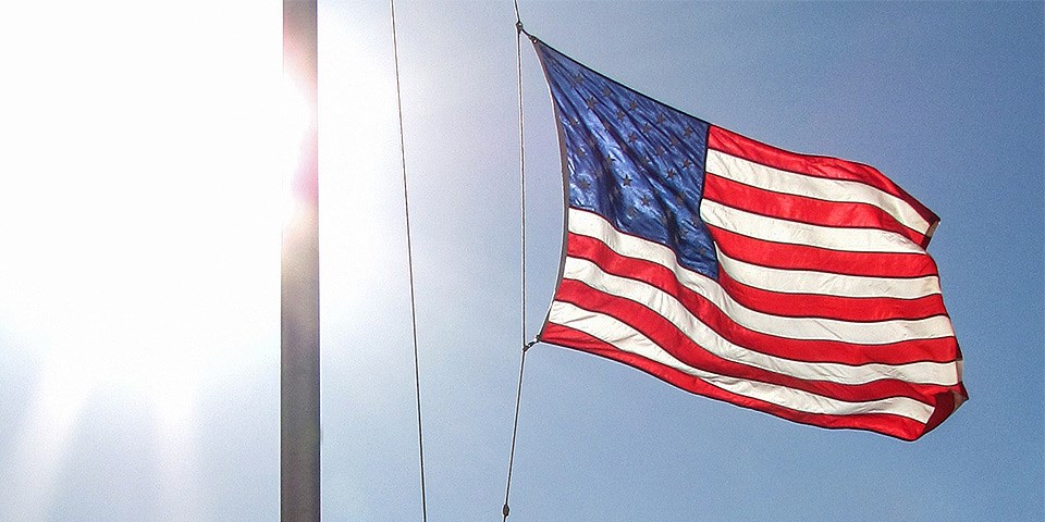 American Flag waving in the breeze with bright sunlight behind the flag pole.