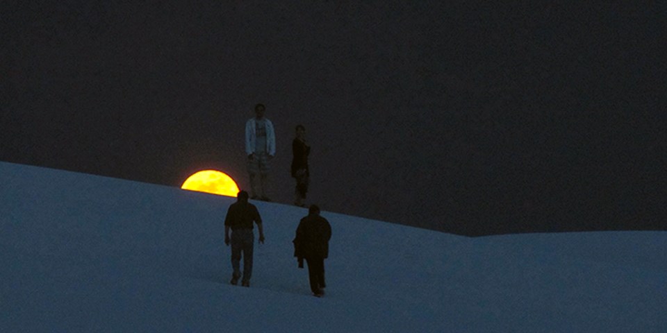 Visitors hiking on the dunes with a full moon on the background.