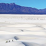 Aerial image of four hikers on white sand with mountains in background