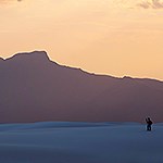 Visitor hiking in the dunefield with the San Andres Mountains on the background.