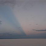 Dune with streaking sunset across blue sky.