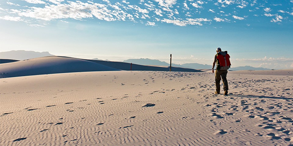 One visitor with backpack hiking toward trail marker on dune.
