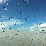 Raindrops on glass with dunes and blue sky in the background