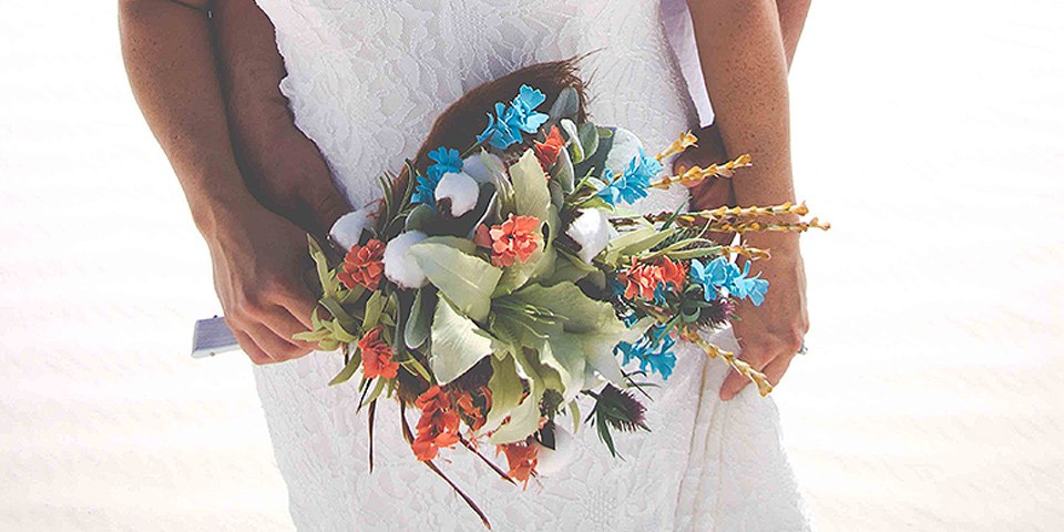 Green, white, and blue flowers in a bouquet held by a women in a white dress