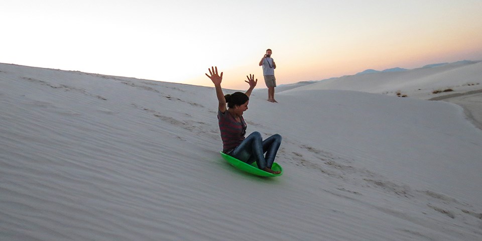 Visitor sledding down dune.