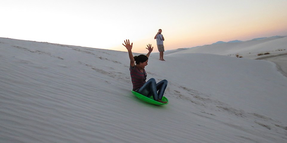 Visitor sledding down dune.