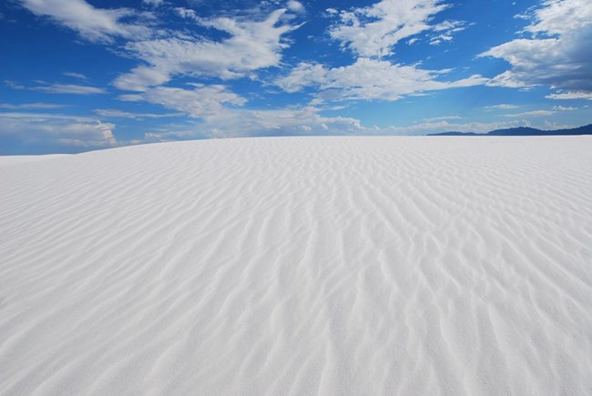 Partly cloudy sky over white sand dunes