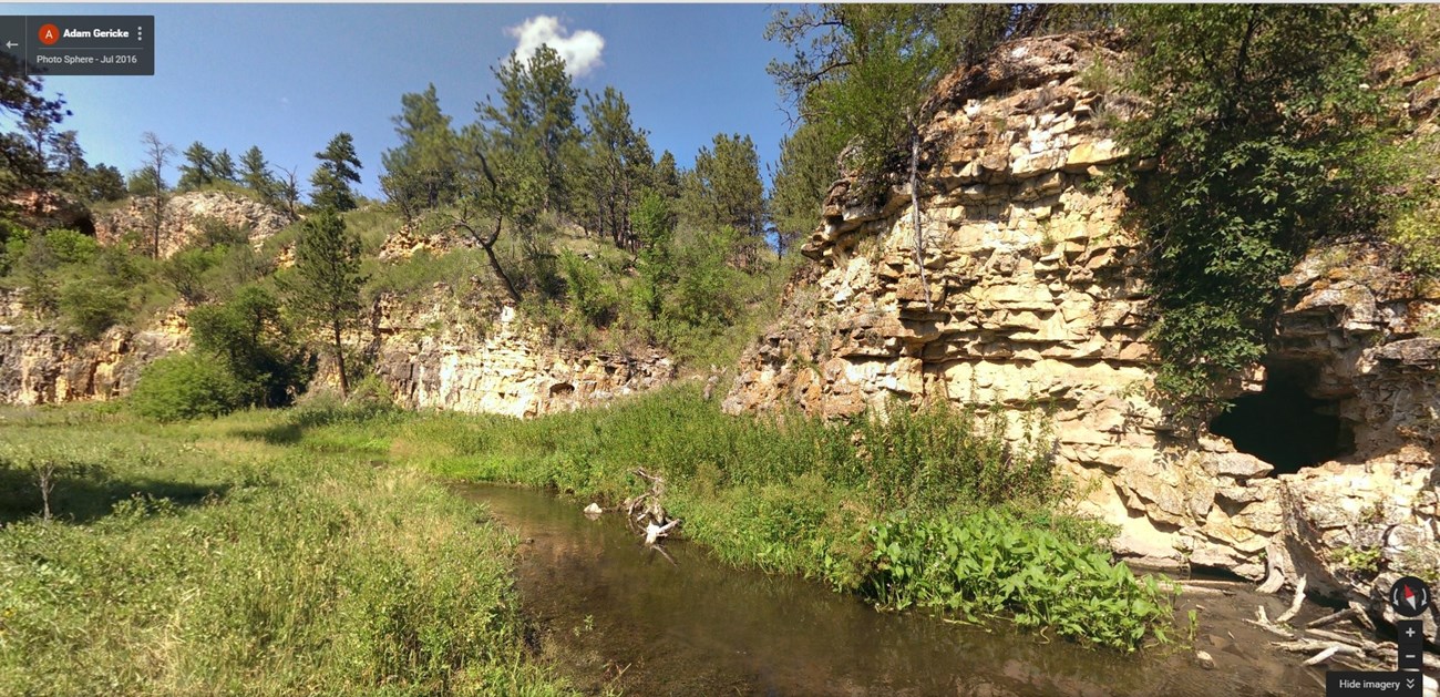 babbling brook in a prairie meadow with a small cave in a nearby cliff face