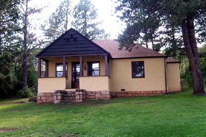 a yellow house with a brown roof and trim with stone steps leading up to a covered porch