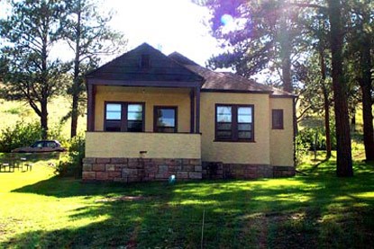 a yellow house with a stone base, a brown roof and trim, and a roofed porch