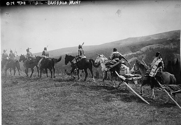black and white photo of a group of native people in traditional clothing on horses riding into the prairie, labeled "on the trail - buffalo hunt"