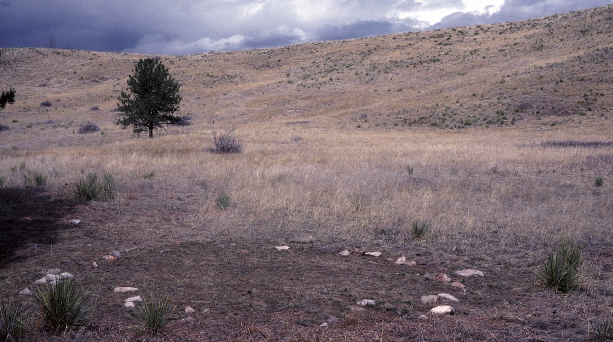 a circle of stones in a brown prairie with a cloudy dark sky