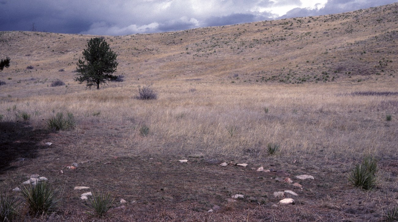 a circle of stones in a brown prairie with a cloudy dark sky
