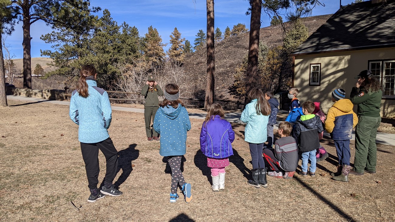A ranger leads a large group of children in an outdoor activity.