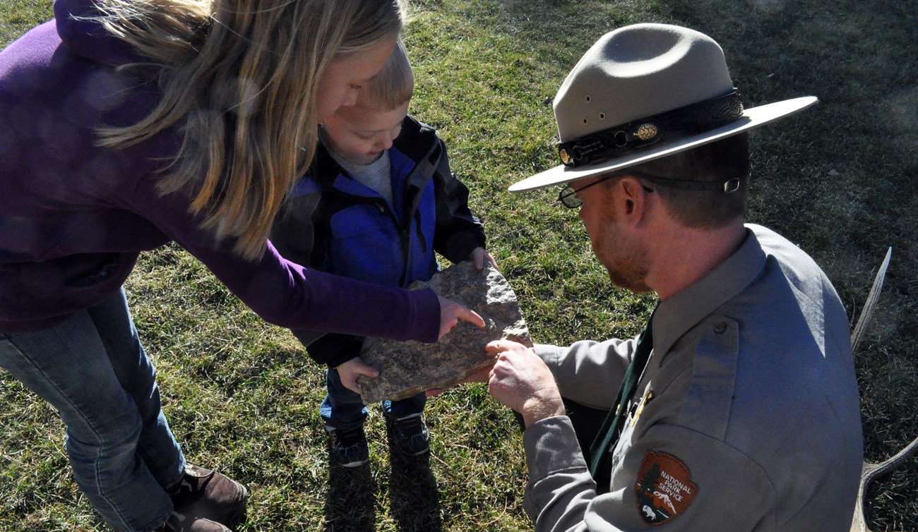 Park ranger showing a young boy and girl fossils in a piece of limestone.