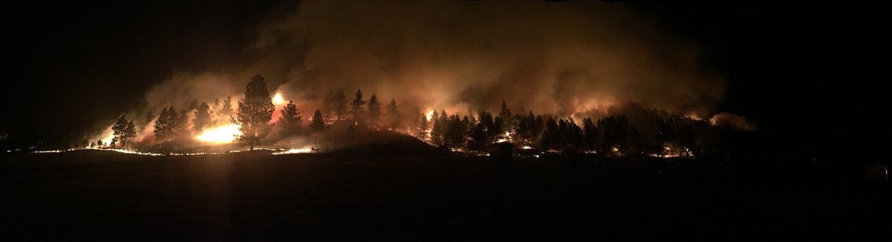An evening photograph of a fire burning a forested hillside