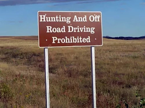Brown sign with white lettering reading "Hunting and Off Road Driving Prohibited"