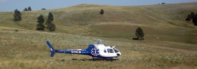 A blue and white emergency helicopter sits in the middle of the prairie.