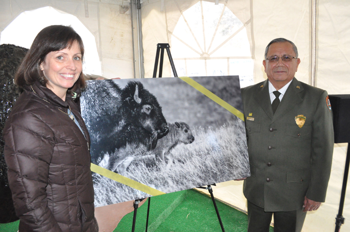 Kelly Keenan Aylward from the Wildlife Conservation Society standing next to a photo of bison. Standing to the right of the bison photo is Superintendent Vidal Dávila.