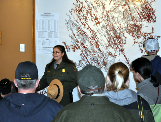 Female ranger standing in front of a map of the cave on the wall with people watching her.