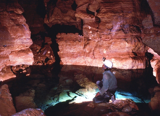 Cave explorer kneeling by underground lake.