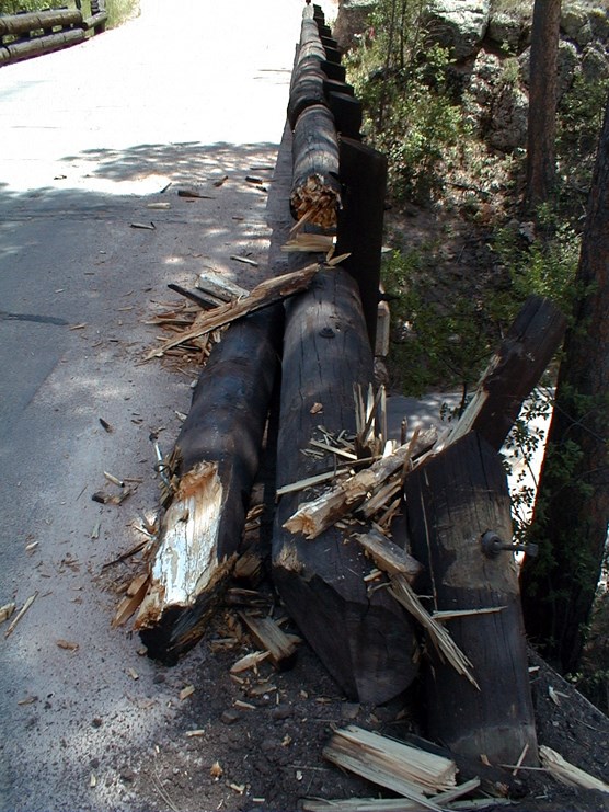 Photograph of vehicle damage caused to Pigtail Bridge on Highway 87. Wood barriers are broken and splintered. Photograph of vehicle damage caused to Pigtail Bridge on Highway 87. Wood barriers are broken and splintered.