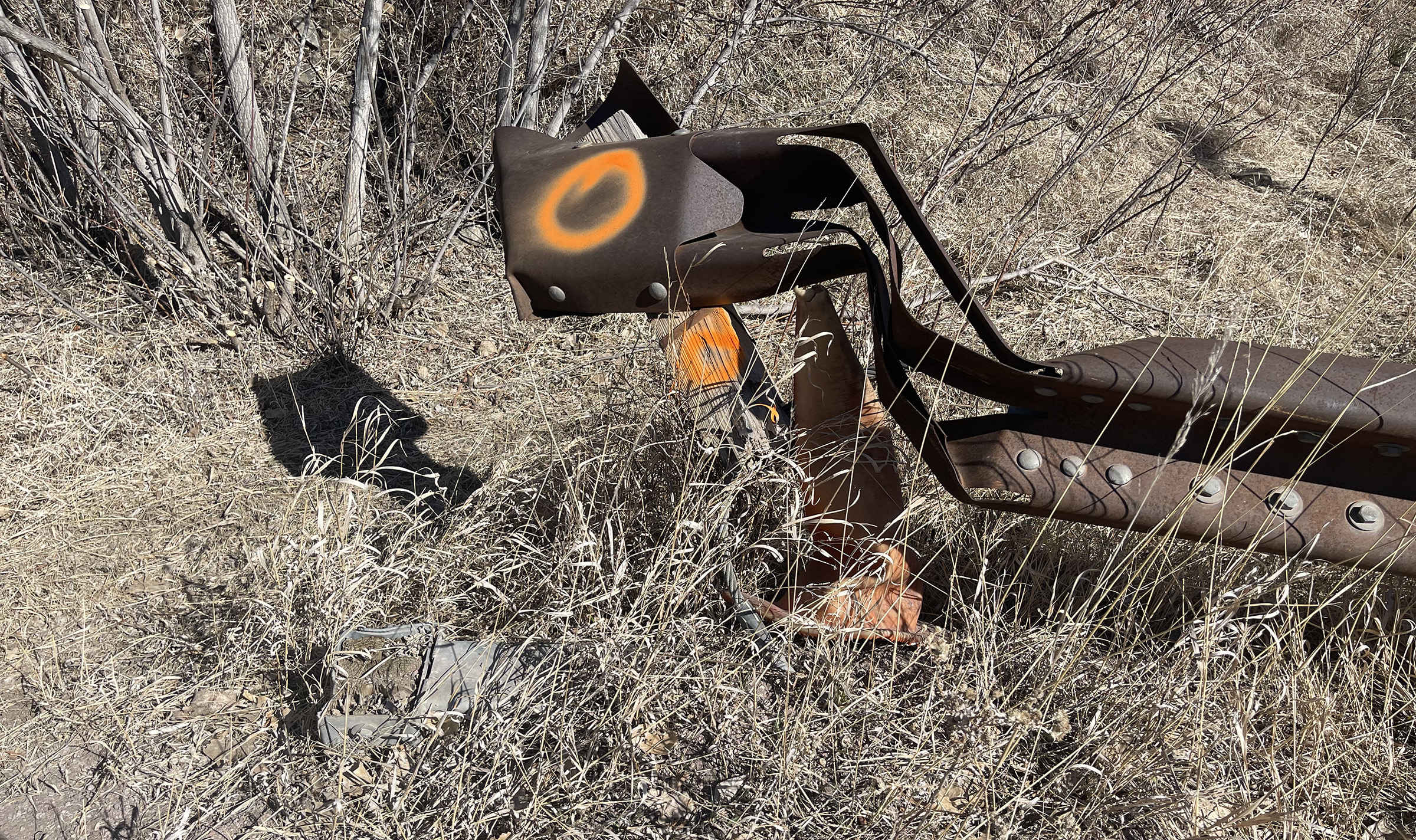 A mangled brown metal guardrail surrounded by prairie grass. A mangled brown metal guardrail surrounded by prairie grass.