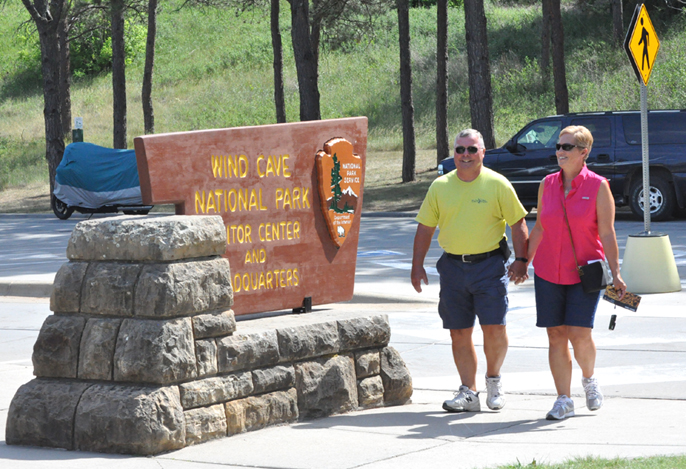 Couple holding hands walking by Wind Cave National Park Visitor Center sign.