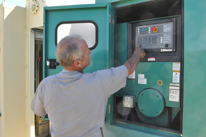 Maintenance specialist Jeff Simmons pointing to button on a backup generator.