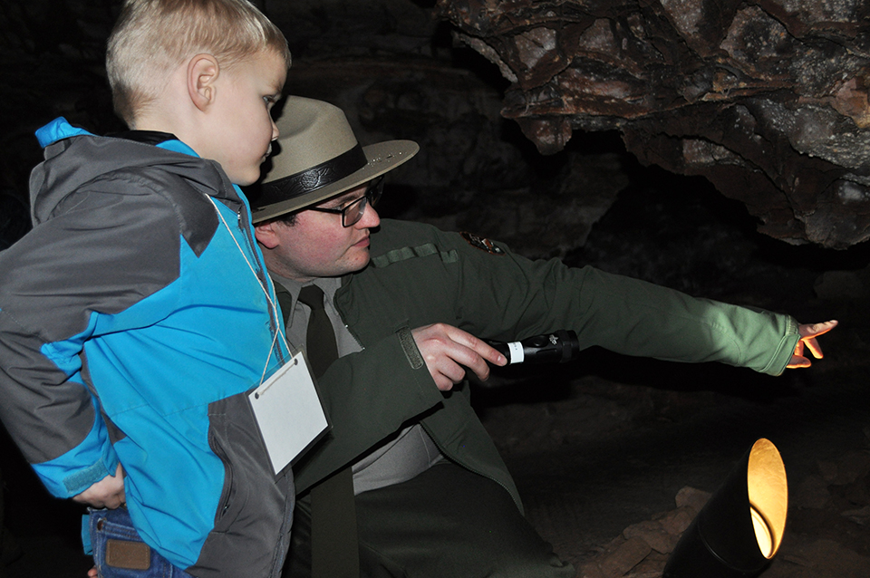 Ranger in cave pointing to a cave formation with a young boy next to him.