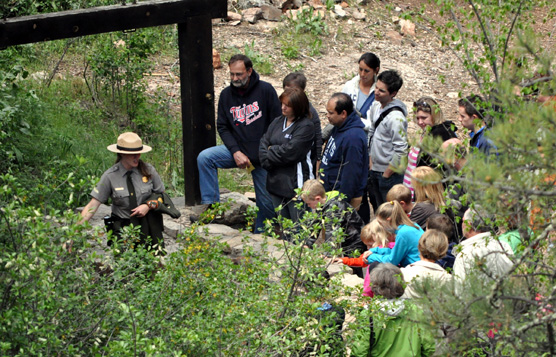 A female ranger stands near the Natural Entrance to Wind Cave as she talks with a tour group.