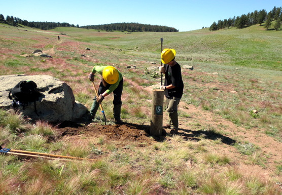 Two SCA crew members out on the prairie installing a wooden post with a number 5 on it.