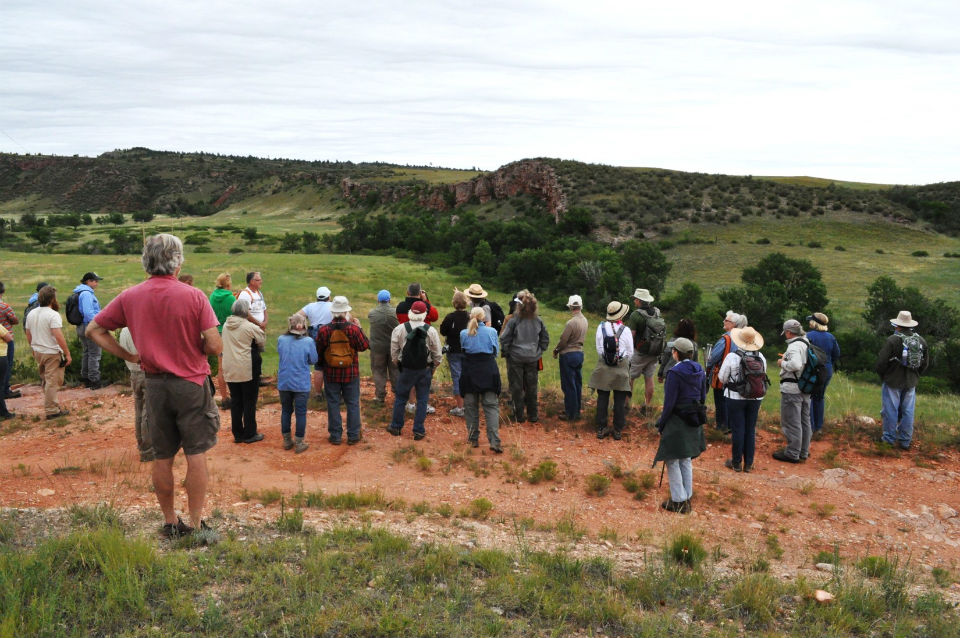Ranger standing in front of a group of people looking at cliff in the background. Ranger standing in front of a group of people looking at cliff in the background.