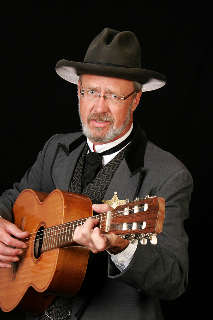 Entertainer Gordy Pratt dressed up like Seth Bullock holding a guitar.