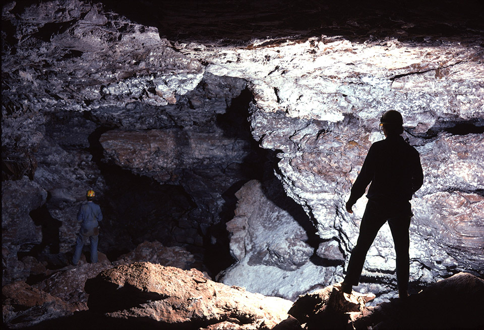 Two cave explores stand in a cave room that leads off into the darkness.