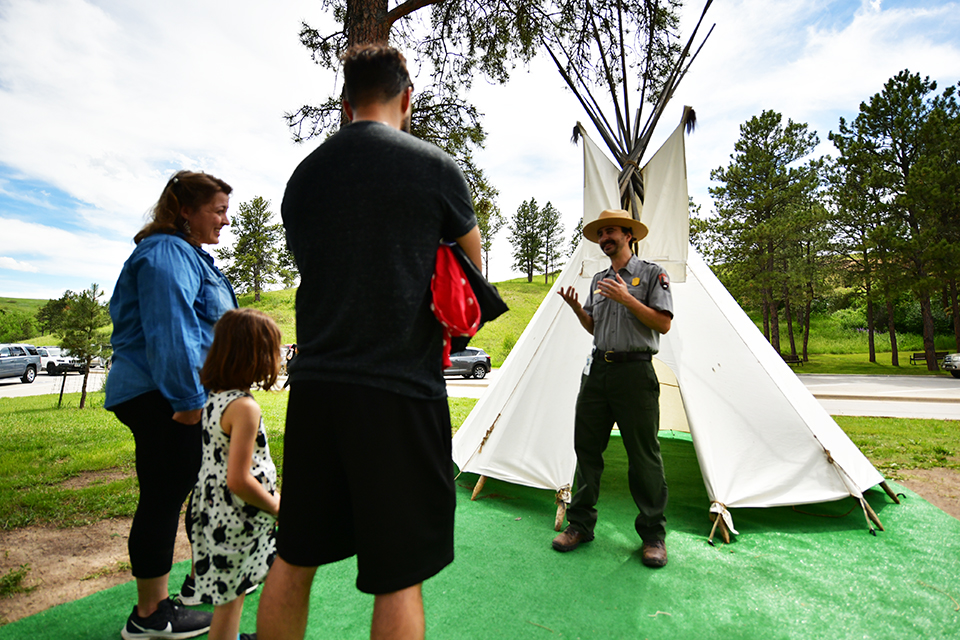 Ranger standing in front of a tipi talking with a family consisting of a man, woman, and child.
