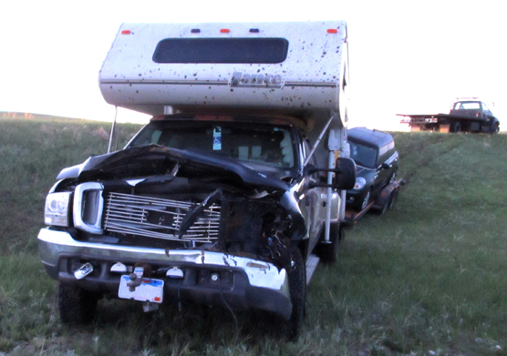 A pickup truck with a camper and towing a trailer has a smashed in front end from hitting bison.
