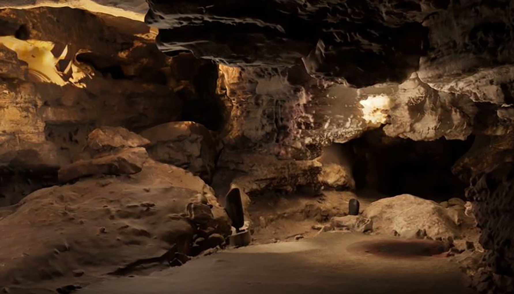 Brown cave walls with lighted areas and shadows along the side of a room.