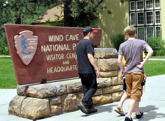 Three visitors walking past Wind Cave National Park's welcome sign in front of the visitor center