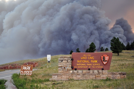 Large column of smoke rising behind park entrance sign.