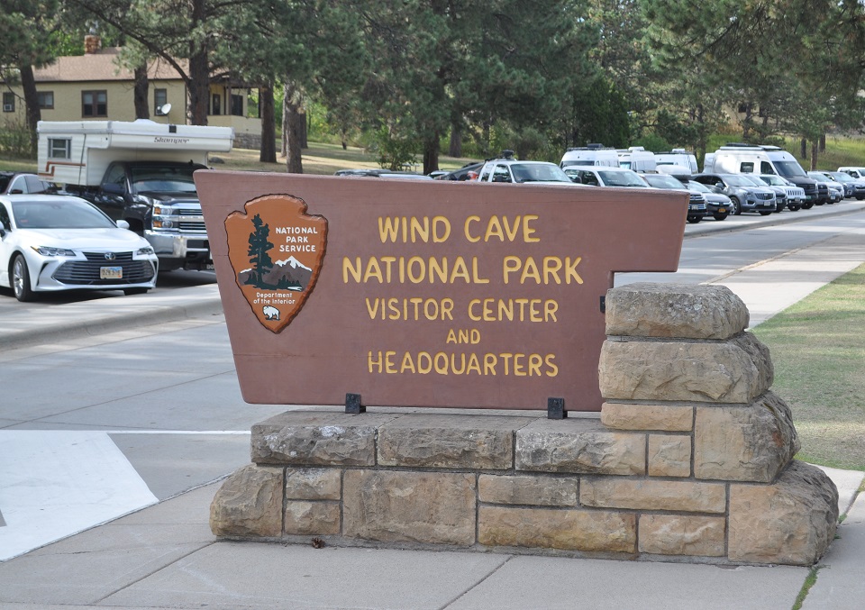Brown wooden sign on a stone base saying Wind Cave National Park Visitor Center and Headquarters