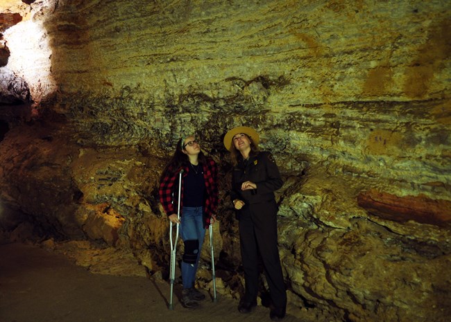 a ranger with a visitor on crutches in a dim cave room