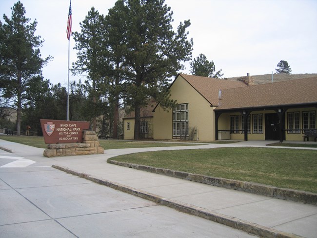 The front exterior of the visitor center with yellow stucco, brown shingles, and numerous tall windows.