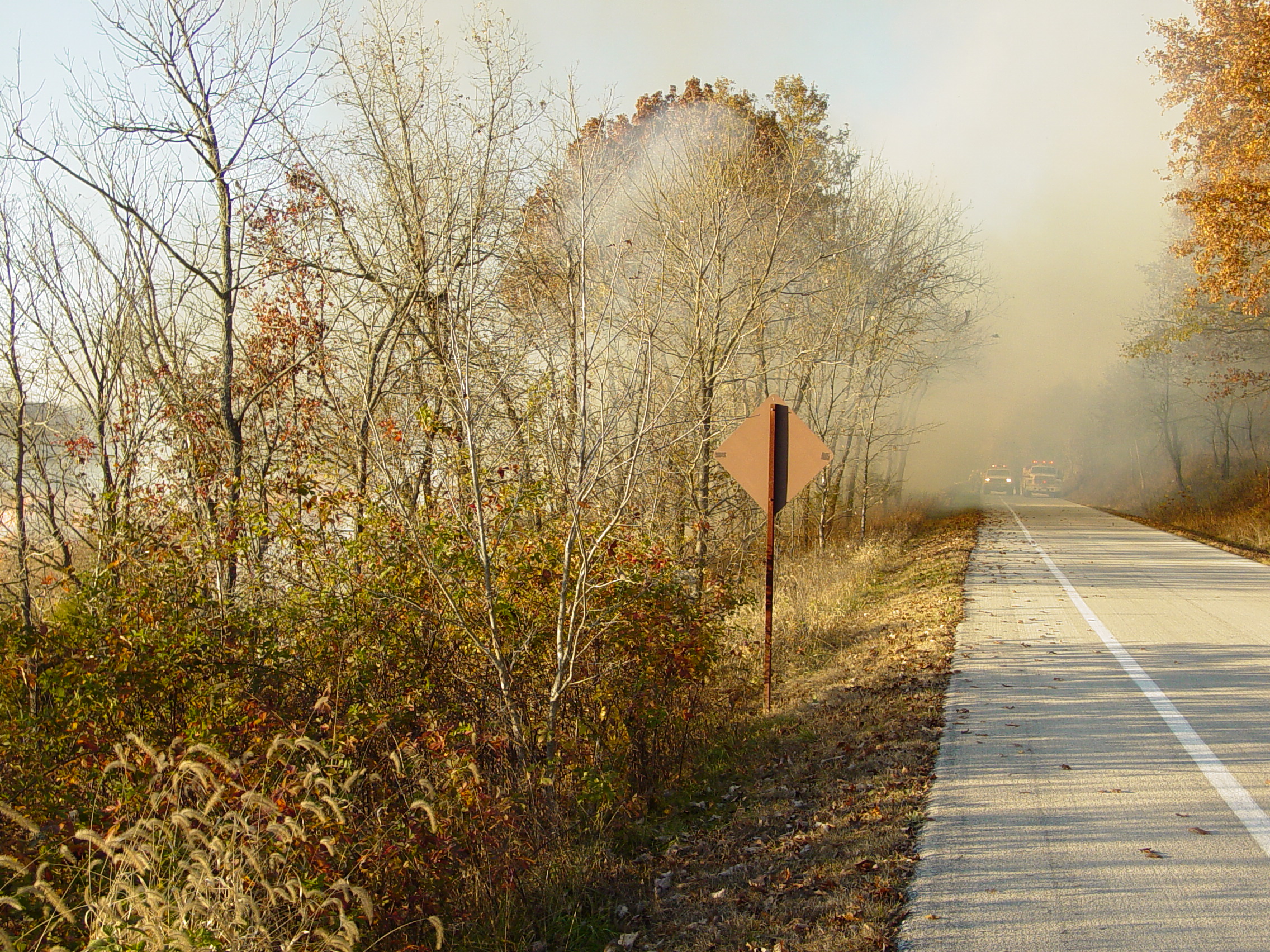 Controlled burn of field with fire and smoke rising. NPS vehicles block tour road for safety.